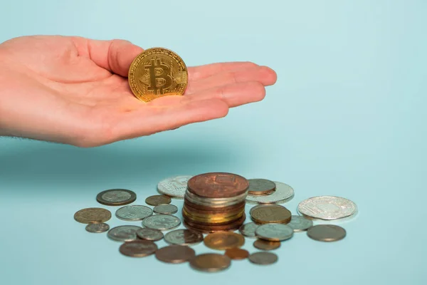 QUIIV, UCRÂNIA - SETEMBRO 22, 2021: visão parcial da mão masculina com bitcoin perto de prata e moedas de ouro em azul, conceito anti-corrupção — Fotografia de Stock