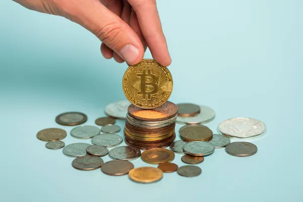 KYIV, UKRAINE - SEPTEMBER 22, 2021: cropped view of male hand near bitcoin and coins on blue, anti-corruption concept — Stock Photo