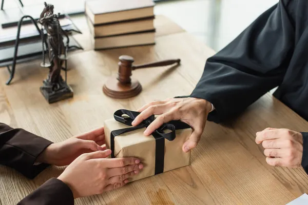 Vista recortada de juez tomando regalo de cliente cerca borrosa mazo en el escritorio, concepto anticorrupción - foto de stock