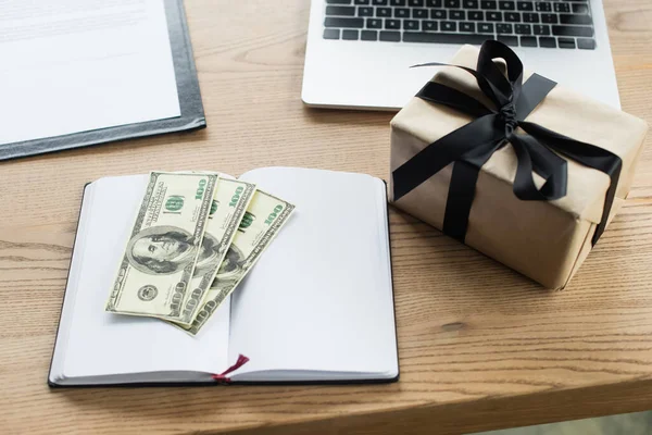 KYIV, UKRAINE - SEPTEMBER 22, 2021: top view of dollars on notebook near gift box and blurred contract, anti-corruption concept — Stock Photo