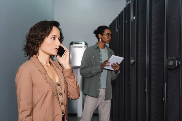 Ingeniero hablando en el teléfono inteligente cerca borrosa programador afroamericano con tableta digital — Stock Photo