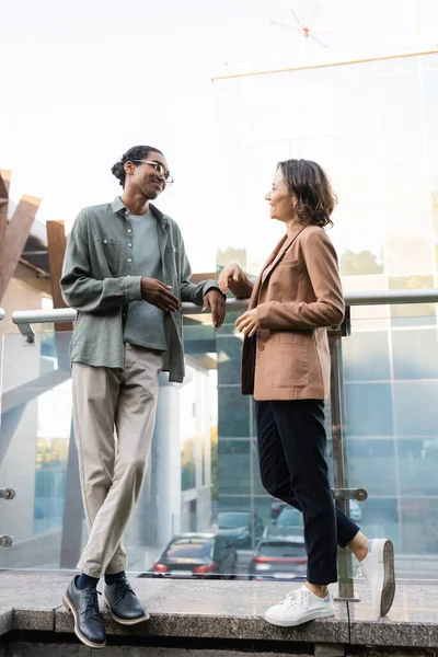 Full length view of interracial couple in trendy clothes talking on balcony — Stock Photo