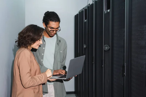 Young interracial engineers using laptop while working in data center — Stock Photo