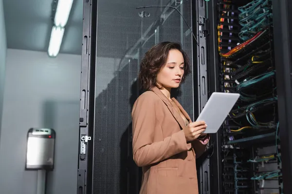 Ingenieur schaut auf digitales Tablet, während er in der Nähe eines offenen Servers im Rechenzentrum steht — Stockfoto