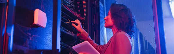 Engineer holding digital tablet while checking server in data center in neon light, banner — Stock Photo