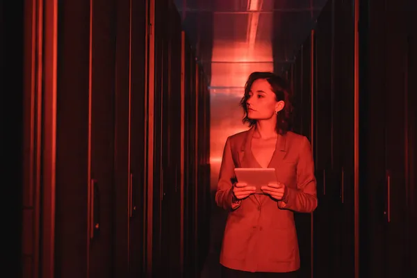 Engineer with digital tablet looking at servers in data center with neon light — Stock Photo