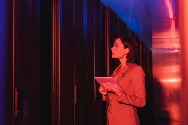 Technician with digital tablet checking servers in data center in neon light — Stock Photo