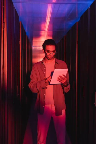 Engenheiro afro-americano em óculos usando tablet digital enquanto trabalhava em data center — Fotografia de Stock