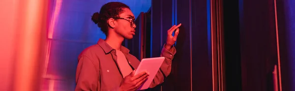 African american technician with digital tablet checking server in data center in neon light, banner — Stock Photo