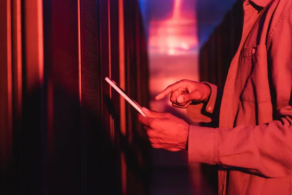 Cropped view of african american engineer pointing at digital tablet while working in data center in neon light — Stock Photo