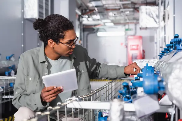 Ingénieur afro-américain avec tablette numérique vérifiant le système de refroidissement dans la salle d'équipement technique du centre de données — Photo de stock