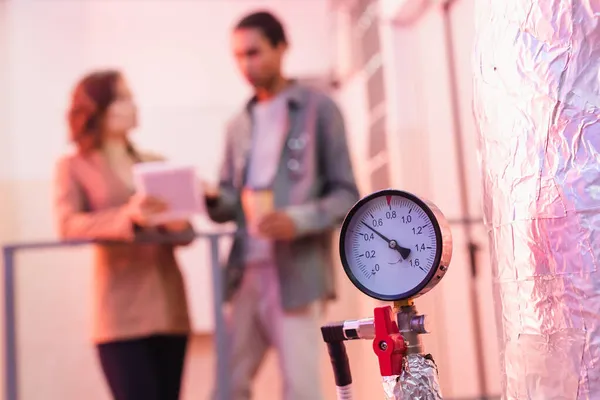 Selective focus of manometer of data center cooling system near blurred interracial engineers — Stock Photo