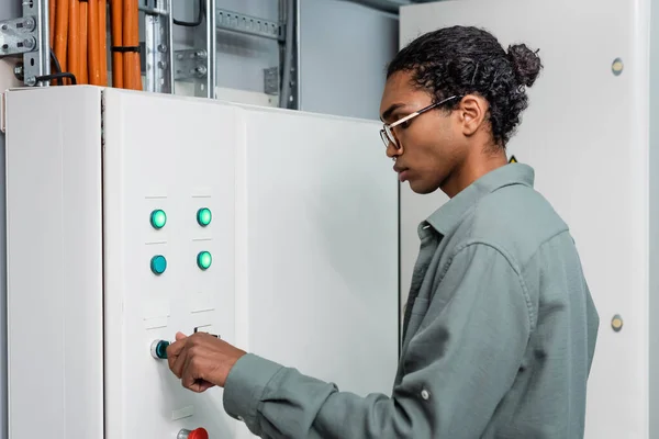 Young african american technician pushing button on switchboard while working in data center — Stock Photo