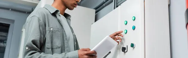 Cropped view of african american administrator with digital tablet pushing button on server in data center, banner — Stock Photo