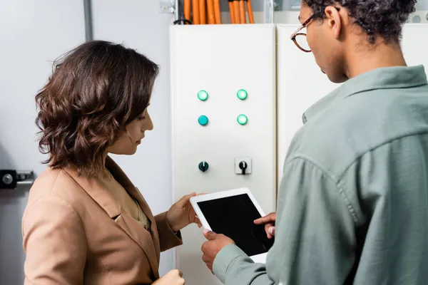 Engenheiro afro-americano apontando para tablet digital próximo a colega e quadro de distribuição do sistema de refrigeração — Fotografia de Stock