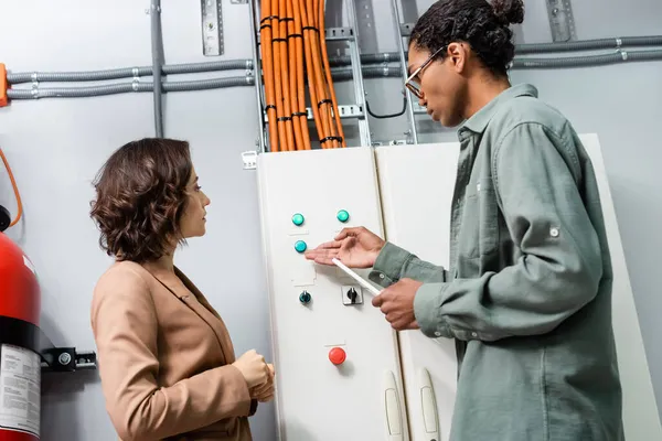 Afrikanisch-amerikanischer Techniker mit digitalem Tablet zeigt auf Schaltschrank, während er mit Kollegen im Rechenzentrum arbeitet — Stockfoto