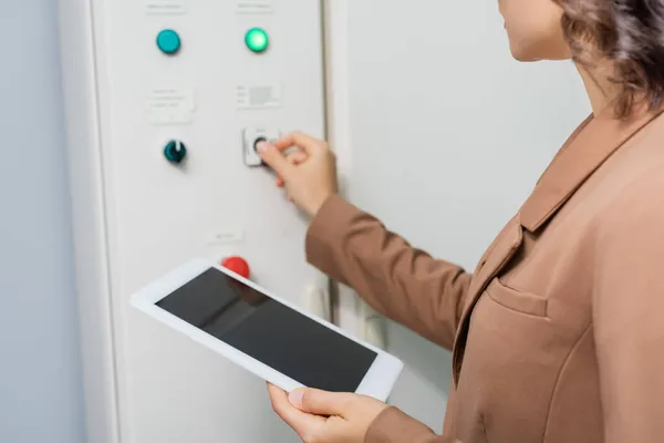 Cropped view of engineer holding digital tablet with blank screen while pushing button on switchboard in data center — Stock Photo