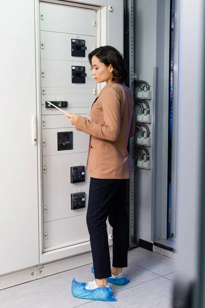 Інженер, який дивиться на цифровий планшет, стоячи біля комутаційної панелі в центрі обробки даних — стокове фото