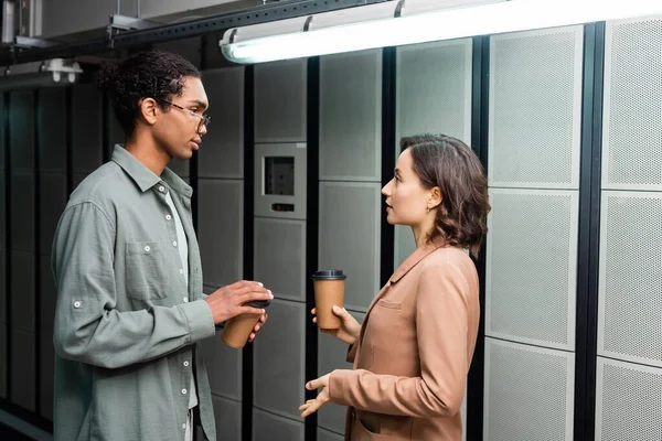 Vista lateral de técnicos multiétnicos con café para ir a hablar en el centro de datos — Stock Photo