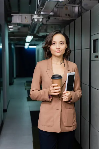 Young engineer with paper cup and digital tablet looking at camera in data center — Stock Photo