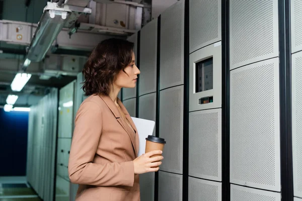 Side view of engineer with digital tablet and coffee to go looking at control panel on server — Stock Photo