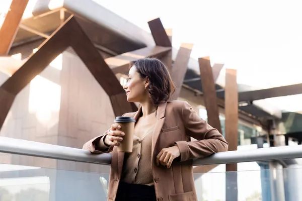 Brunette woman in beige blazer looking away on balcony of building outdoors — Stock Photo