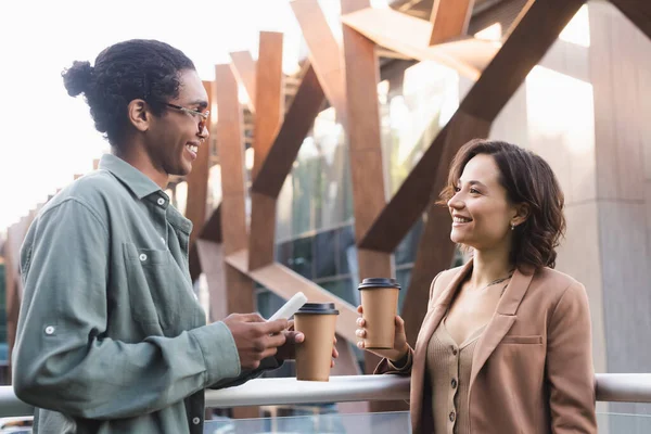 Smiling african american man with smartphone talking with young woman outdoors — Stock Photo