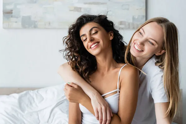 Alegre lesbiana mujer abrazando feliz novia en dormitorio - foto de stock