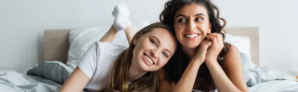 Веселые лесбиянки, лежащие на кровати дома, баннер — стоковое фото
