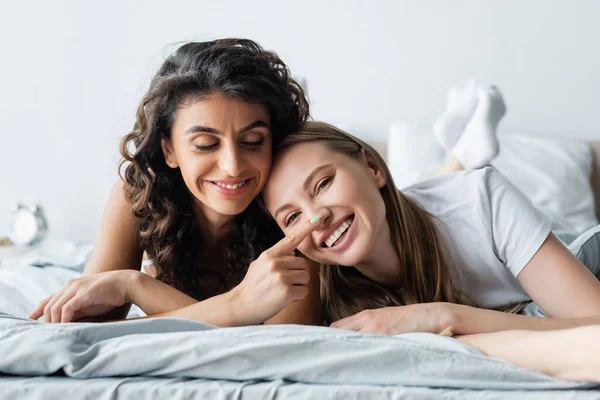 Alegre mulher lésbica deitada na cama e tocando o nariz da namorada — Fotografia de Stock