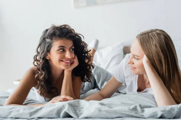 Feliz casal lésbico olhando um para o outro e deitado na cama — Fotografia de Stock