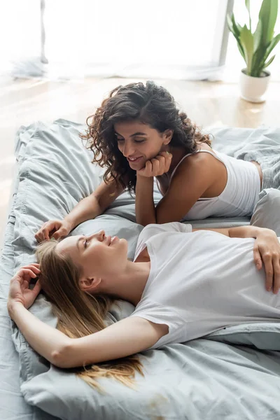 Высокий угол обзора положительной лесбийской пары лежа и глядя друг на друга в спальне — стоковое фото