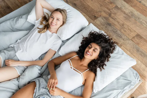 Top view of cheerful lesbian couple lying on bed — Stock Photo