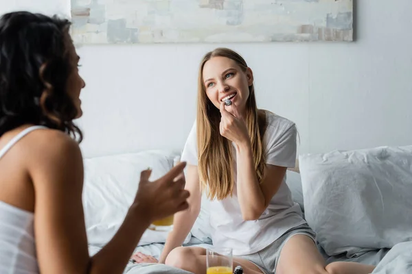 Junge Frau isst Brombeere und schaut Freundin mit einem Glas Orangensaft an — Stockfoto