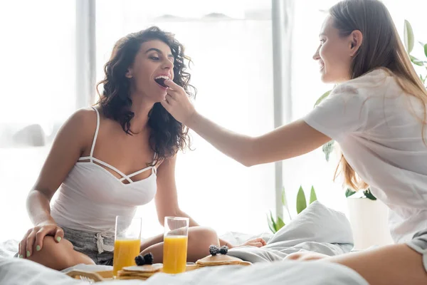 Junge Frau füttert Freundin mit Brombeere in der Nähe Tablett mit Frühstück — Stockfoto