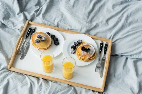 High angle view of blackberries on tasty pancakes near glasses on orange juice on tray — Stock Photo