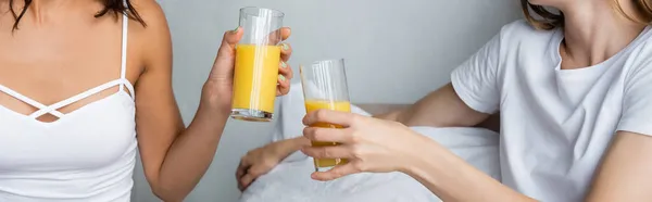 Vista recortada de las mujeres tintineo vasos con jugo de naranja, bandera - foto de stock