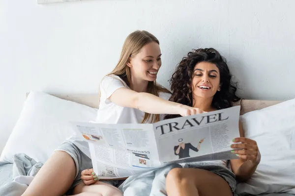 Alegre pareja lesbiana leyendo periódico de viaje en el dormitorio - foto de stock