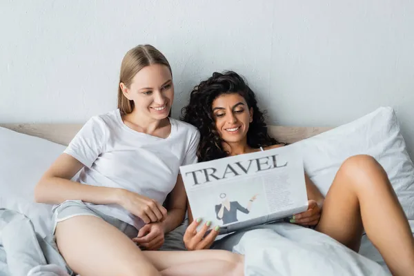 Feliz pareja lesbiana leyendo periódico de viaje en el dormitorio - foto de stock