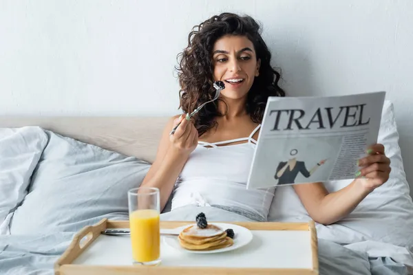 Mulher feliz e encaracolado segurando garfo com amora e ler jornal de viagem — Fotografia de Stock