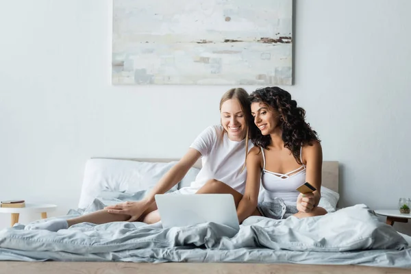 Mujeres lesbianas felices mirando el ordenador portátil mientras que hace compras en línea en el dormitorio — Stock Photo