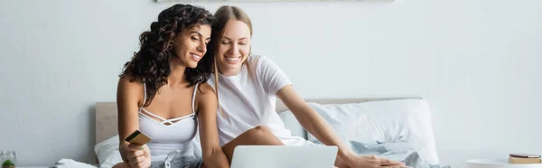 Happy lesbian couple looking at laptop while online shopping from home, banner — Stock Photo