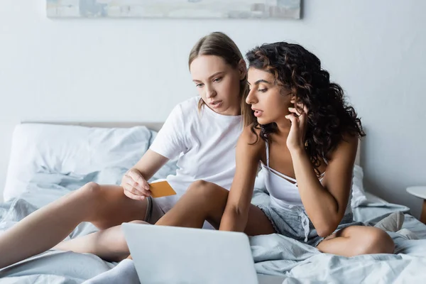 Молодая лесбийская пара смотрит на ноутбук в то время как онлайн покупки из дома — стоковое фото