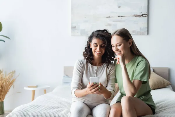 Pregnant woman using smartphone near happy girlfriend in bedroom — Stock Photo