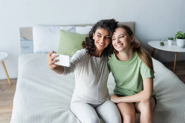 Mujer embarazada tomando selfie con novia feliz en el dormitorio - foto de stock