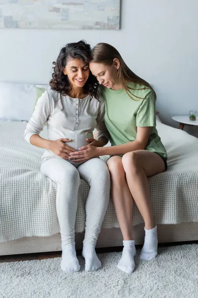 Fröhliche Frau berührt Bauch der schwangeren Freundin im Schlafzimmer — Stockfoto