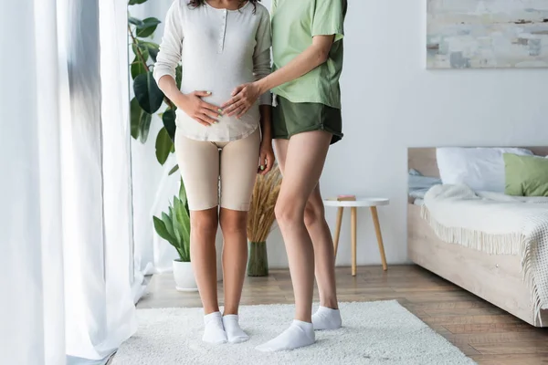 Cropped view of woman touching belly of pregnant girlfriend in bedroom — Stock Photo