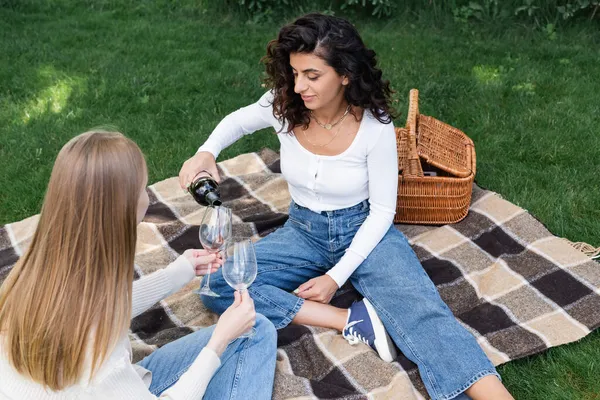 Jovem mulher derramando vinho tinto em copo de namorada durante piquenique — Fotografia de Stock