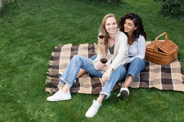 Giovane coppia lesbica che tiene bicchieri di vino rosso durante il picnic nel parco — Foto stock