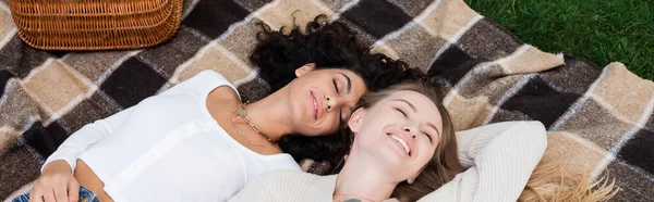 Happy lesbian couple lying on plaid blanket during picnic, banner — Stock Photo